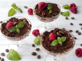 Dessert Tiramisu in glass goblet with mint coffee beans and fresh raspberries on white wooden table