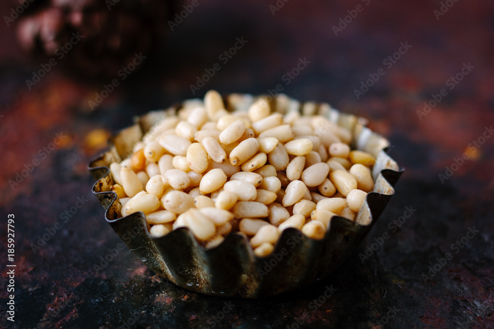 Poster pine nuts in a metal bowl over dark background.