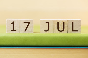 Wooden cube shape calendar for JUL 17 on green book, table. 