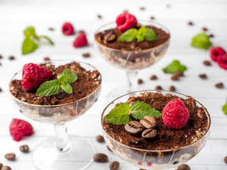 Dessert Tiramisu in glass goblet with mint coffee beans and fresh raspberries on white wooden table