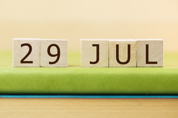 Wooden cube shape calendar for JUL 26 on green book, table. 