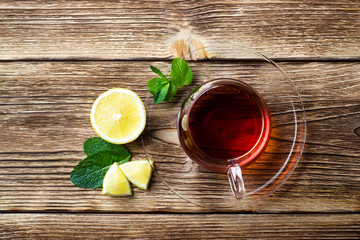 Glass cup with tea, mint and lemon on wooden rustic background. Top view with copy space.