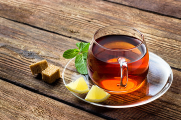 Glass cup with tea, mint and lemon on wooden rustic background.