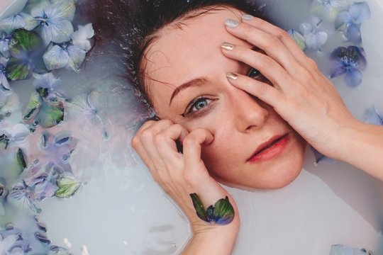 Overhead view of a young woman lying in a milky bath with flowers at a spa