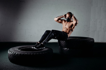 Man wearing an elevation mask while doing sit ups on tires