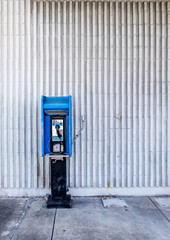 blue public pay phone against a white wall