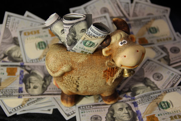 A piggy bank with stuck bills stands on scattered dollars. Close up of dollars. The American currency is in the piggy bank. Money on a black background.