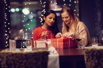 Two adolescent women going through the menue  in a fancy restaurant, while drinking a glass of red wine and laughing and talking, maybe gossiping