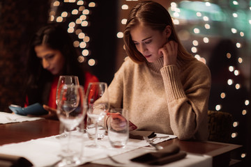 Two adolescent women going through the menue  in a fancy restaurant, while drinking a glass of red wine and laughing and talking, maybe gossiping