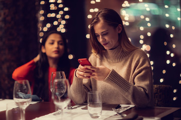 Two adolescent women going through the menue  in a fancy restaurant, while drinking a glass of red wine and laughing and talking, maybe gossiping