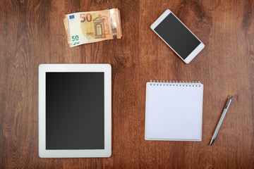 worktop top view. white tablet and smartphone with a blank screen, money, notepad with pen and money
