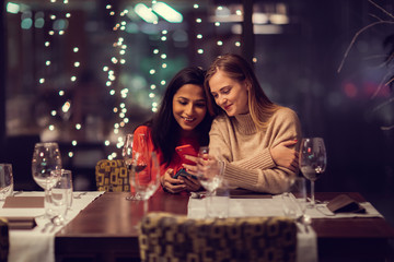 Two adolescent women going through the menue  in a fancy restaurant, while drinking a glass of red wine and laughing and talking, maybe gossiping