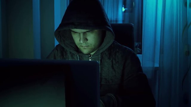 4k footage of young male hacker in hoodie working on laptop at home in night