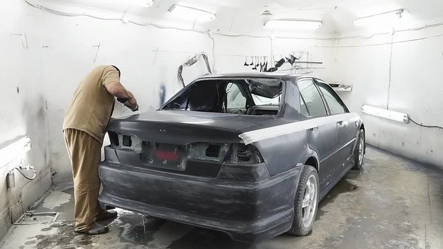 professional repairman worker in automotive industry sanding metal caer roof before painting at bodywork