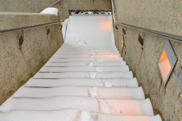 Footprints in fresh snow, going up an outdoor staircase in a concrete stairwell
