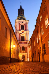 Fototapeta na wymiar Cobbled street and baroque tower of the former monastery in the evening in Poznan.