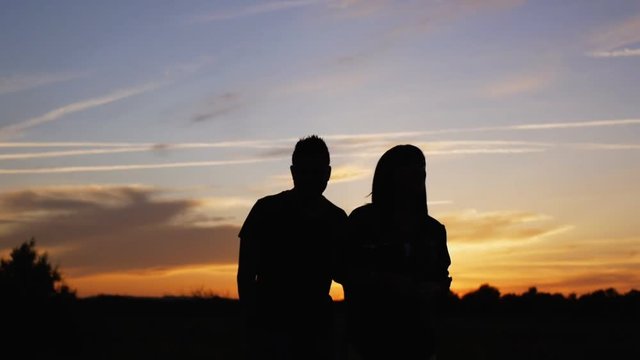 Silhouette of musicians singing and dancing. Man and woman sing and dance waving arms outdoors on a sunset sky background.