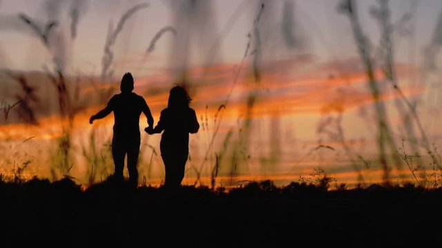 Silhouette of walking couple. Man and woman run hand in hand approaching on a sunset sky background.
