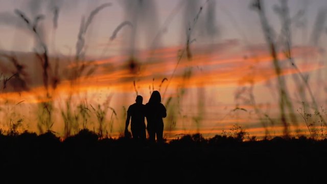 Silhouette of walking couple. Man and woman going away on a sunset sky background. Slow motion