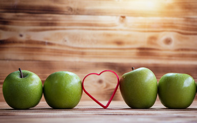 Closeup green apple stack in a row and red heart put at the middle of row, on wooden timber board,blurry light around.