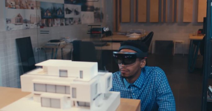 Young confident African American black male architect working on a private house project in the office, studying mansion model. 4K UHD
