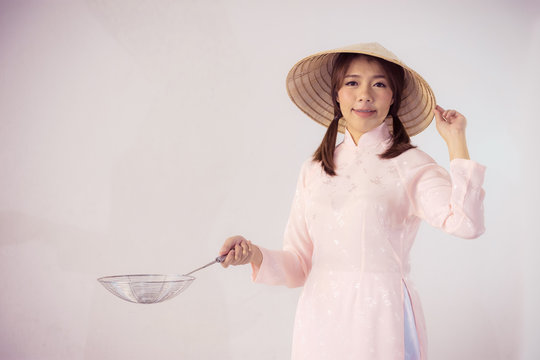 beautiful woman in pink dress and vietnam hat holding cooking utensils.