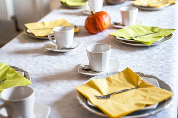 Beautiful festive dinner table colorful yellow fall helloween pumpkin decoration coffee mugs saucers plates and spoons