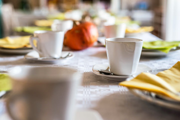Beautiful festive dinner table colorful yellow fall helloween pumpkin decoration coffee mugs saucers plates and spoons