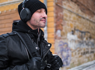 middle aged man walking by the street in winter time and listening to the music via headphones