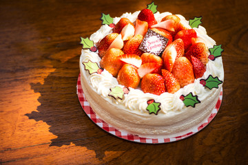 Homemade sponge strawberry cake for season greetings on wooden table and touched by evening light. Dressing composed of fresh strawberries, cream and green sugar leaves.