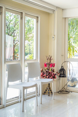 white chairs and artificial flowers with lamp by the windows.
