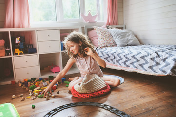 child girl cleaning her room and organize wooden toys into knitted storage bag. Housework and help...