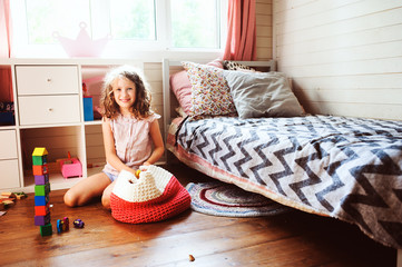 child girl cleaning her room and organize wooden toys into knitted storage bag. Housework and help...