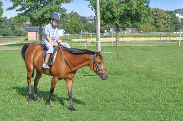 ein 9 jähriger Junge reitet allein auf dem Reitpaltz auf einem braunem Pferd