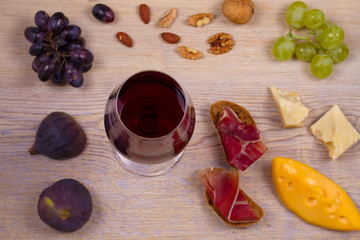 Wine with cheese, prosciutto, figs, nuts and grapes on wooden background. Wine and food concept, overhead, horizontal
