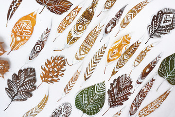 A lot of autumn dry leaves with white hand-drawn ethnic patterns. Top view.