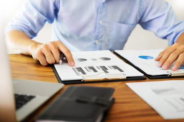 business men working on wooden desk(table) with notebook computer paper, pencil and hand in office, financial concept.