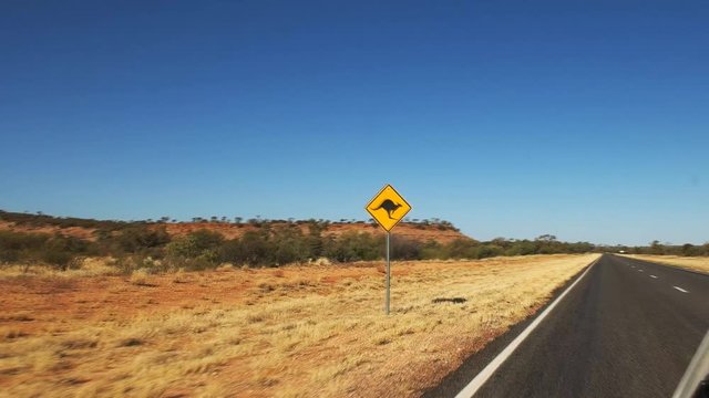 a car drives past a kangaroo road sign in outback australia