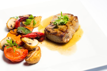 meat with grilled vegetables on a plate on white background