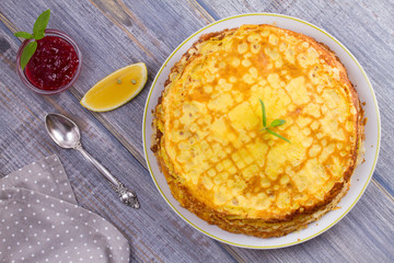 Stack of thin pancakes, crepes on white plate, cup of tea and berry jam, overhead