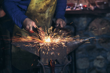 The blacksmith manually forging the molten metal on the anvil in smithy with spark fireworks, close...