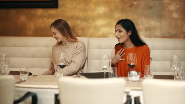 two adolescent women sitting in a fancy restaurant, drinking a glass of red wine and exchainging gifts on a special occasion, maybe birthday or christmass