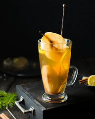 Hot spicy festive drink! Mulled white wine with spicy pears, ginger, honey, cinnamon and lemon in a glass with a vintage spoon on a dark wooden background. Winter xmas holidays concept.