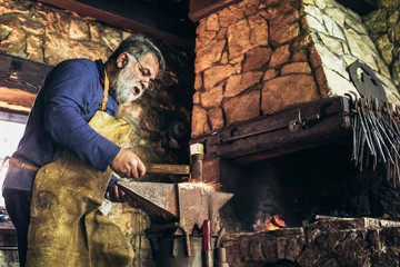 Fototapeta na wymiar Senior blacksmith forge iron at work