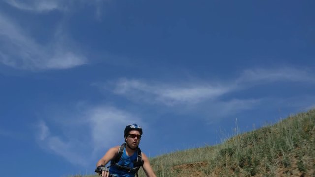 Fat bike also called fatbike or fat-tire bike in summer driving on the road. The guy rides by the hill on a sand clay path, behind him the shore by the sea. Slow motion shooting 180fps.