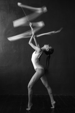 Beautiful Woman Gymnast With A White Ribbon On A Black Background.