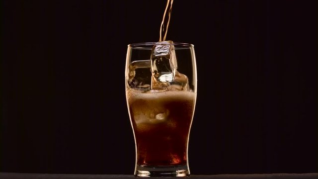 Cola poured into a glass with ice it foams to form a foam cap. Black background