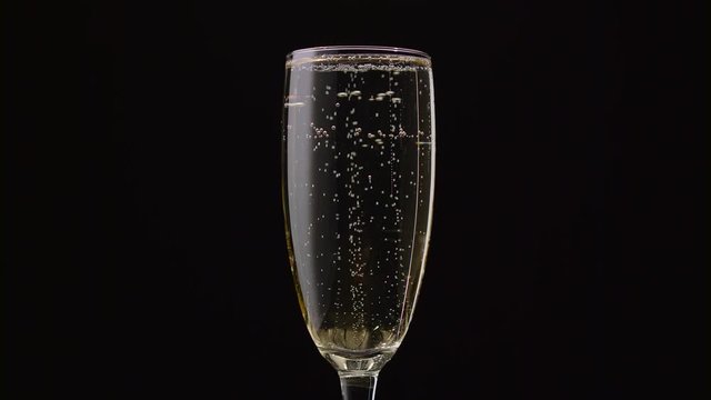 Glass of champagne with a rotating bubbles inside. Black background. Close up