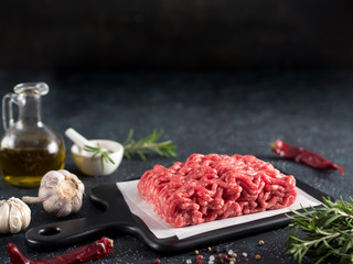 Fresh raw minced beef on backing paper and cutting board and ingredients over black cement...