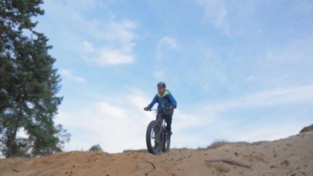 Fat bike also called fatbike or fat-tire bike in summer riding in the sand hill. The guy is riding a bicycle on a sand hill. He rides and sinks in the sand. He tries to perform tricks.